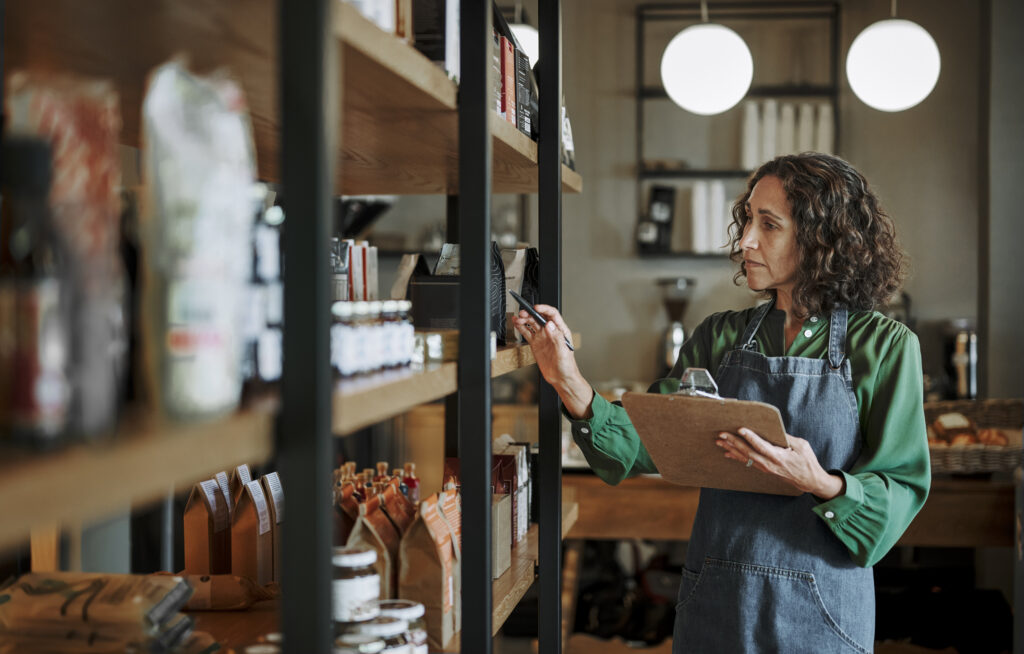 Mature deli owner taking inventory on store shelves using a clipboard