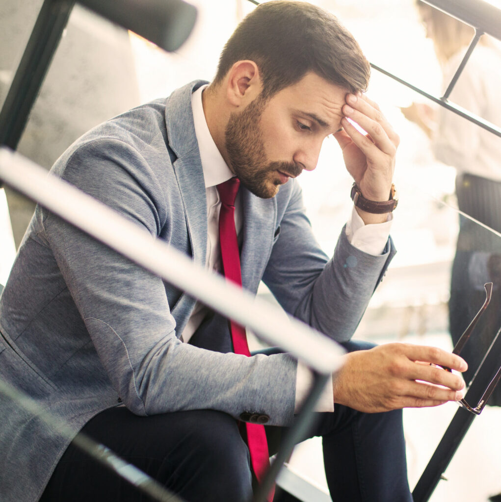 Man sitting down, rubbing his head, looking stressed and burned out