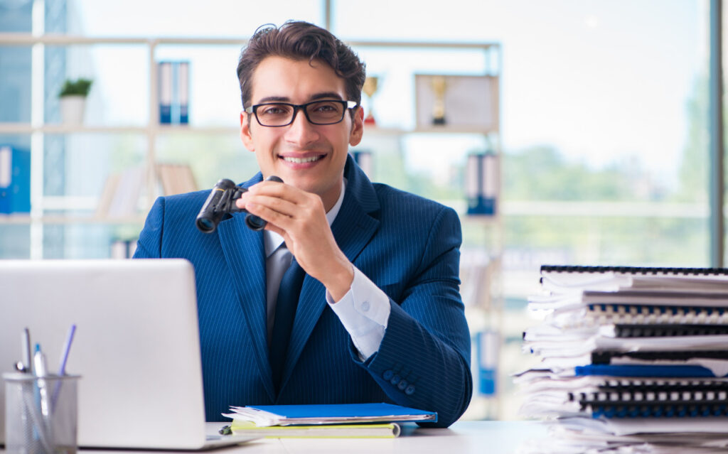 man sitting at his computer with binoculars