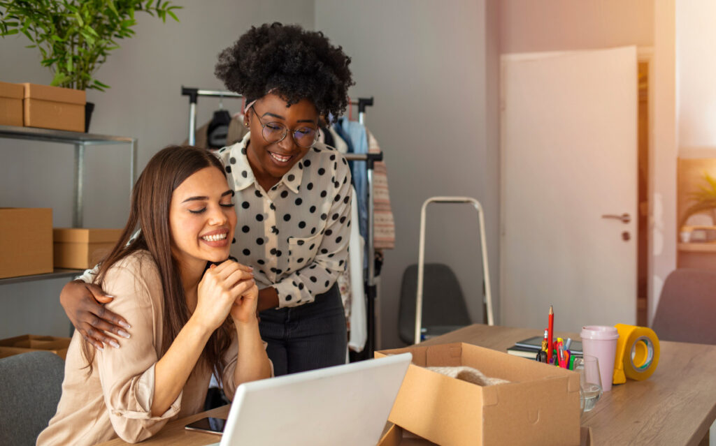 woman standing over another woman at her desk in front of her laptop