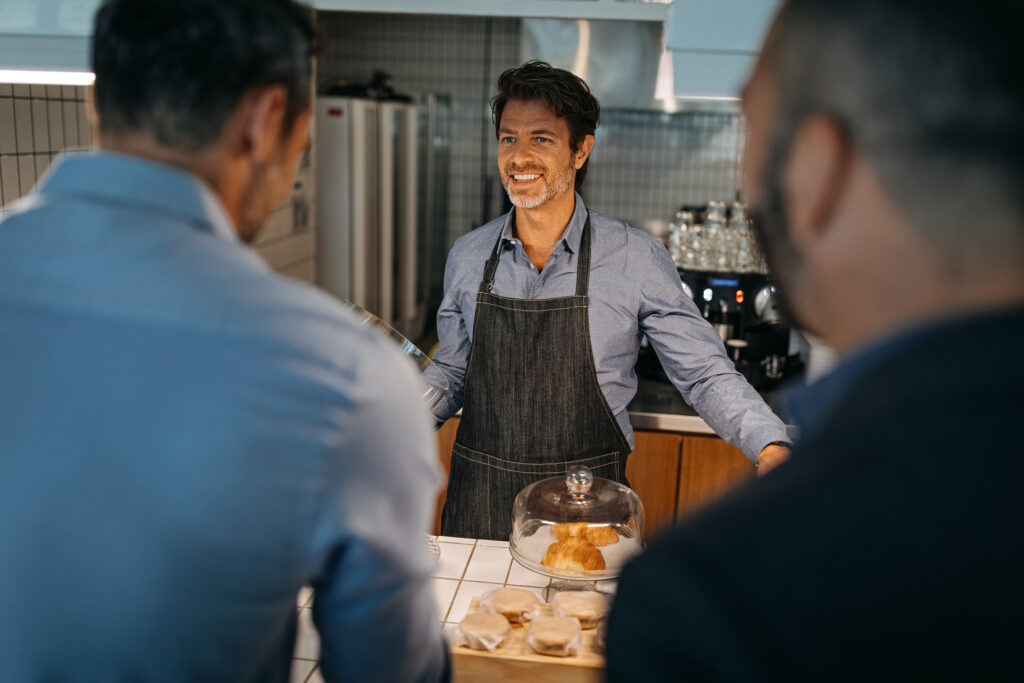 Happy entrepreneur talking with customers at his bakery shop