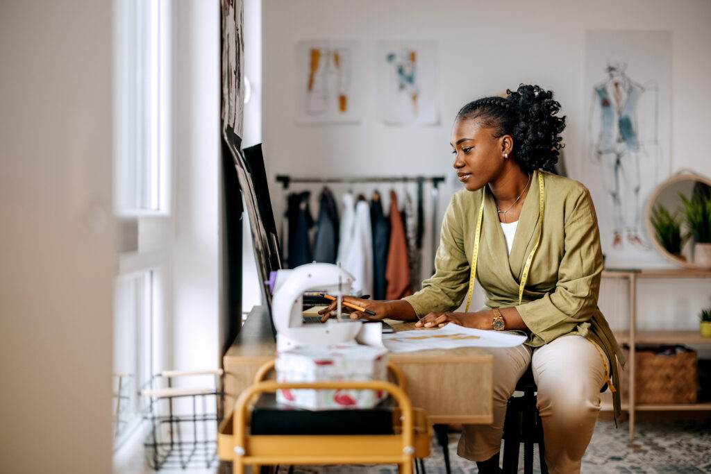 Young beautiful female clothing designer drawing sketches at workshop