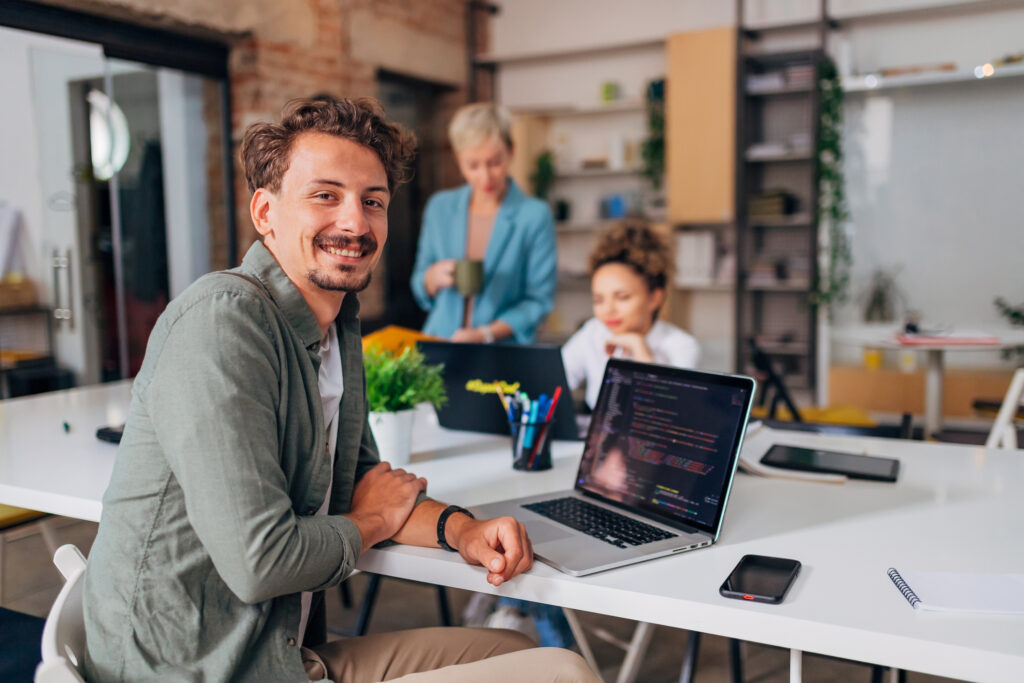 A cheerful man sits at a conference table across from his two female colleagues